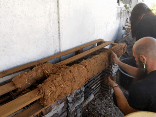 Personnes appliquant un mélange de terre et de paille sur des structures en bois dans un espace de stockage.