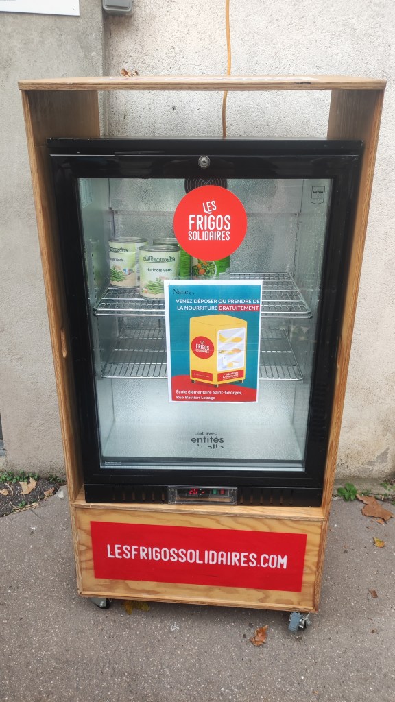 Frigo solidaire placé devant l'école élémentaire Saint-Georges à Nancy, avec un panneau indiquant la possibilité de déposer ou prendre de la nourriture gratuitement.