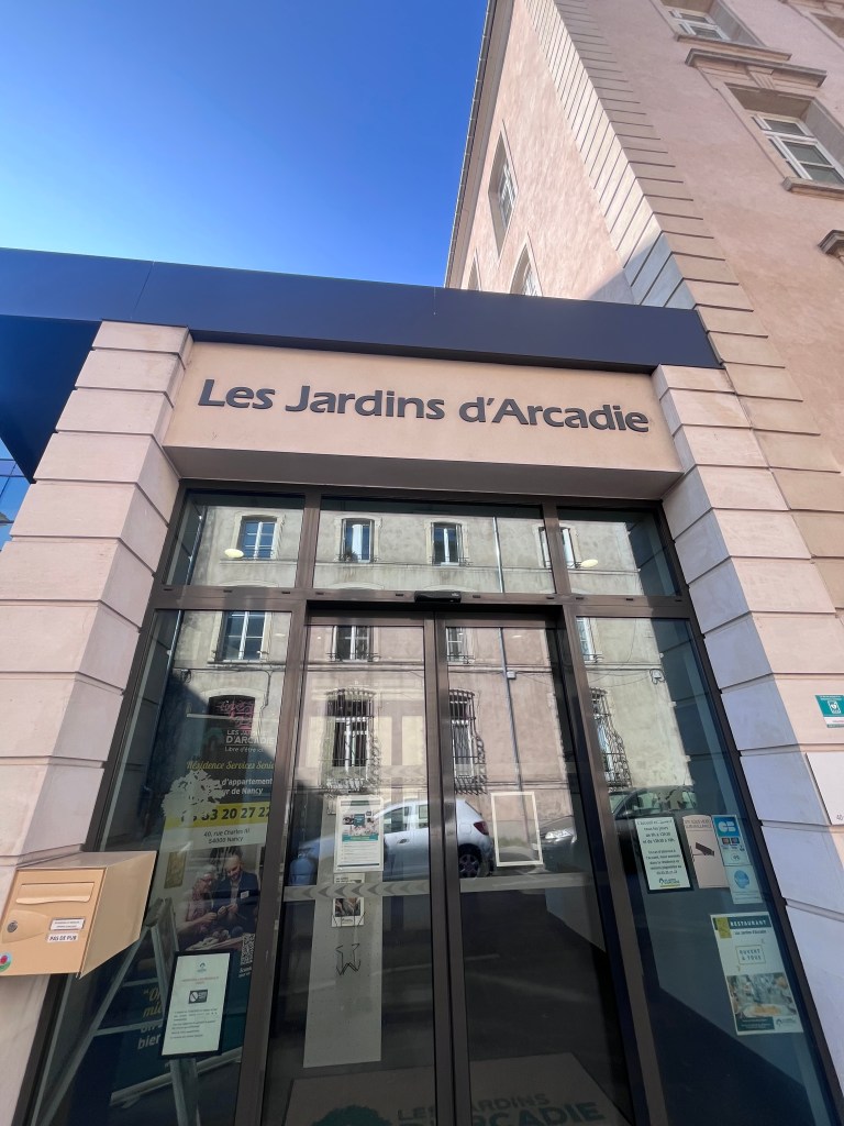 Entrée de Les Jardins d'Arcadie, avec des détails architecturaux modernes et une vitrine donnant sur la rue.