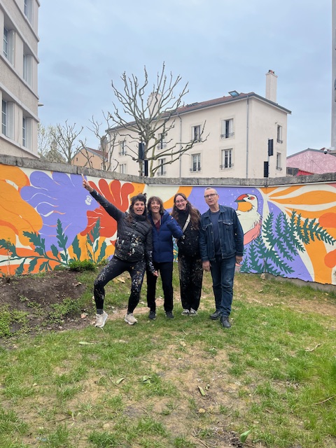 Quatre personnes posent devant une fresque colorée sur un mur, avec des motifs floraux et un oiseau.
