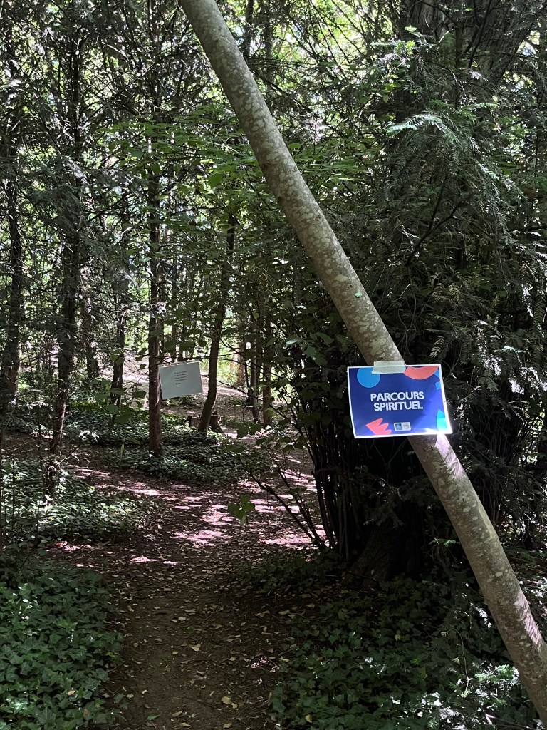 Un chemin à travers une forêt avec des panneaux indiquant un parcours spirituel.