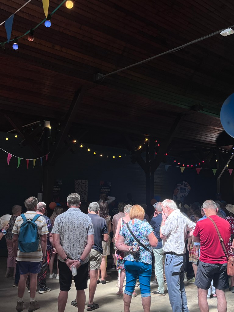 Une foule de personnes se tient à l'intérieur d'un bâtiment animé, décoré de guirlandes de lumières et de fanions multicolores.