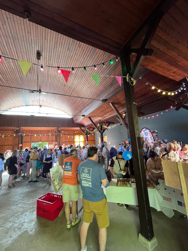 Une vue d'un marché ou d'un événement avec une grande foule, décoré de guirlandes colorées et de lumières, dans un bâtiment au plafond en bois.