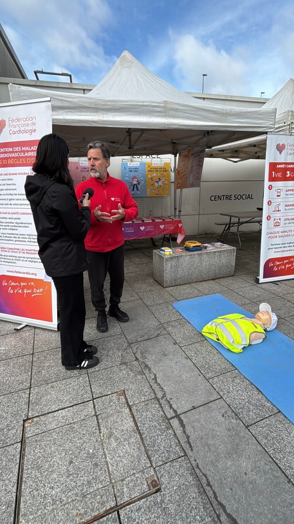Un homme explique des techniques de secours à une femme, près d'un mannequin de réanimation cardiaque, lors d'un événement de sensibilisation à la santé cardiovasculaire.