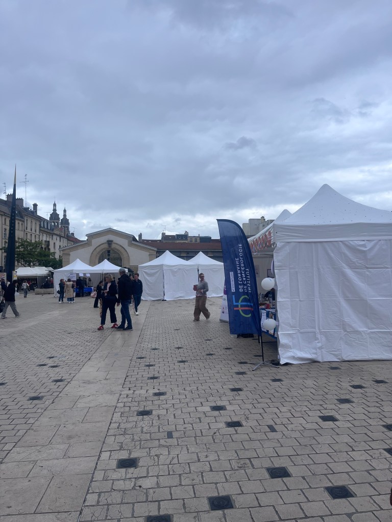 Un marché en plein air avec des tentes blanches, des gens se promenant sous un ciel nuageux.