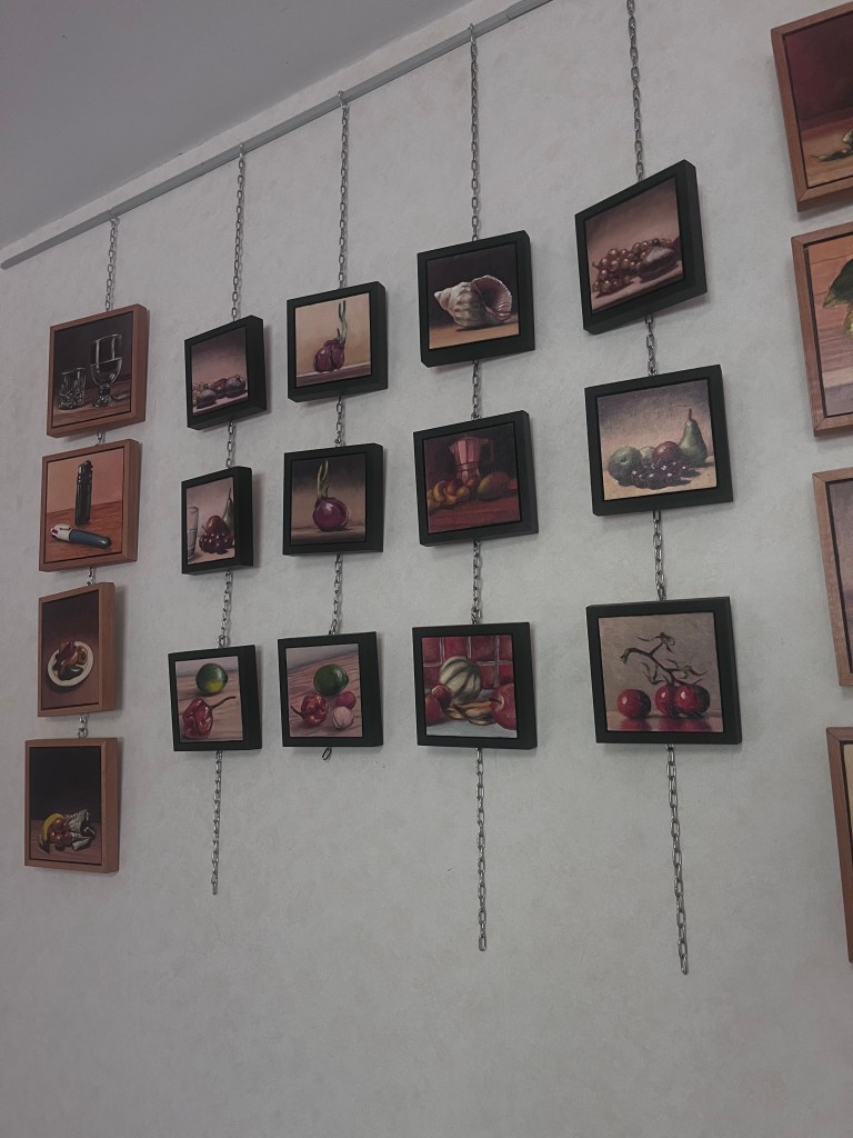 Mur décoré avec des tableaux représentant des fruits, des légumes et des objets de cuisine, accrochés avec des chaînes.