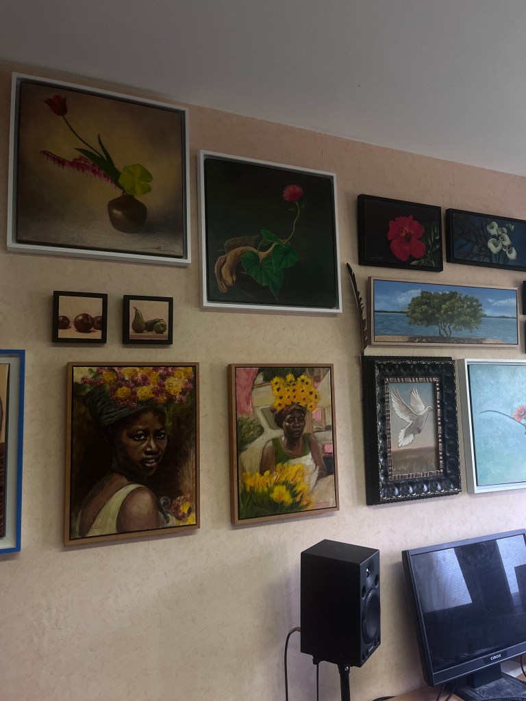 Mur décoré avec plusieurs peintures, y compris des portraits de femmes africaines et des natures mortes de fleurs et de fruits.
